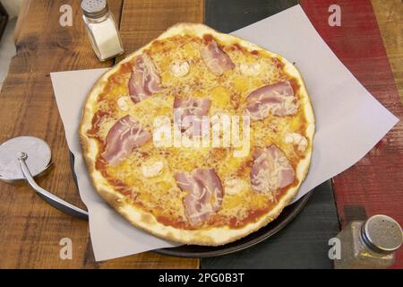 Una meravigliosa pizza a base di crosta media e sottile con pancetta, vari tipi di formaggio e pomodoro su un colorato tavolo di legno Foto Stock