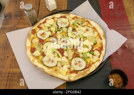 Una meravigliosa pizza a base di crosta media e sottile con vari tipi di verdure fresche e pomodoro su un colorato tavolo di legno Foto Stock