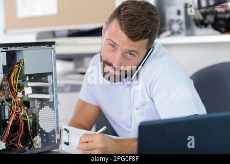 tecnico al telefono che ripara un pc Foto Stock