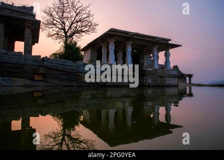 Rovine di vecchi templi con riflessione in uno stagno sul colle Hemakuta a Hampi. Hampi, la capitale dell'impero Vijayanagar, è un sito patrimonio dell'umanità dell'UNESCO Foto Stock