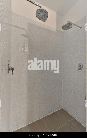 un bagno piastrellato bianco con soffione doccia e tenuto a mano fauziato sulla parete di fronte alla vasca Foto Stock