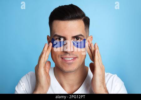 Uomo che applica sotto gli occhi patch su sfondo azzurro Foto Stock