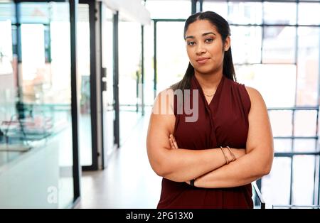 Una persona che è tranquillamente fiduciosa rende il leader migliore. Ritratto di una giovane donna d'affari in piedi con le braccia incrociate in un ufficio. Foto Stock