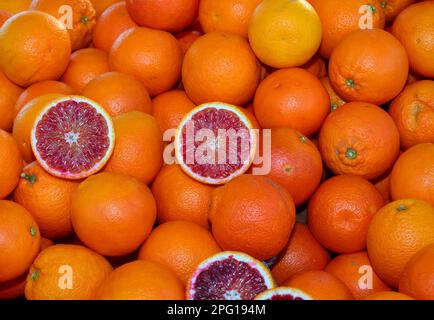 sfondo di arance arance mature e due metà si aprono per vedere il contenuto succoso in vendita al fruttivendolo Foto Stock