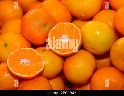 sfondo di molte clementine o tangerini arancioni mature e alcuni tagliati a metà Foto Stock