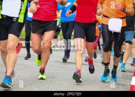 Gruppo intenzionalmente sfocato di atleti con abbigliamento sportivo corrono durante la corsa in strada asfaltata Foto Stock