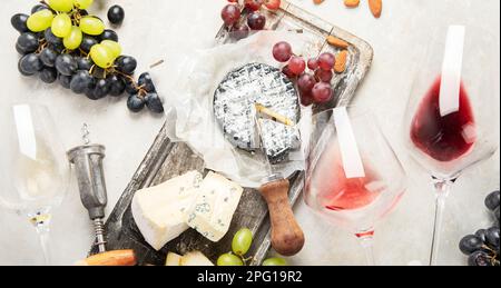 Vino rosa e rosso servito con formaggi, noci, uva e bicchieri di vino. Deliziosi spuntini enogastronomici assortiti serviti a bordo. Piatto stendere su un bianco ba Foto Stock