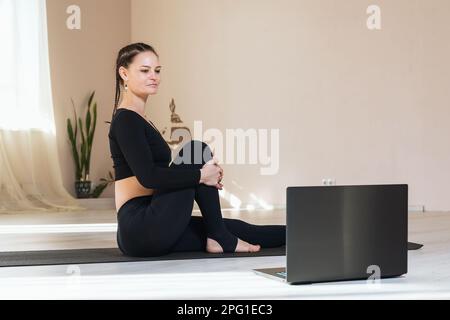 Donna che pratica yoga, guardando le lezioni online mentre si siede su un tappetino in una sala fitness Foto Stock