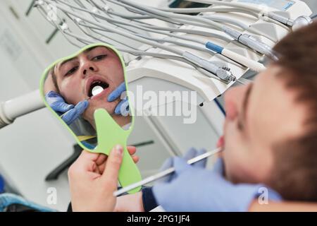 Il dentista esamina la condizione dei denti con l'aiuto dello specchio dentale nei pazienti Foto Stock