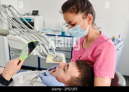 Il dentista esamina la condizione dei denti con l'aiuto dello specchio dentale nei pazienti Foto Stock