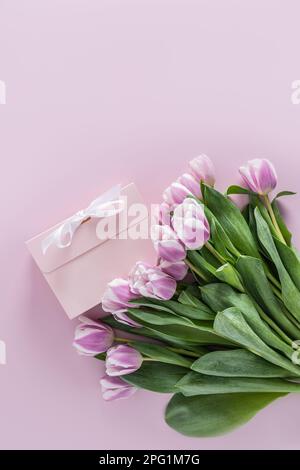 bel bouquet primaverile di tulipani su sfondo viola con una scatola regalo con un nastro bianco. vista verticale. spazio per il testo Foto Stock