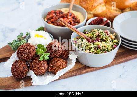 Tavolo tradizionale Shabbat: pane challah, falafel, insalata di quinoa, hummus su un asse di legno. Concetto di cibo israeliano. Foto Stock