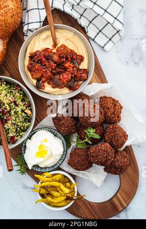 Tavolo tradizionale Shabbat: pane challah, falafel, insalata di quinoa, hummus su un asse di legno. Concetto di cibo israeliano. Foto Stock