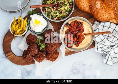 Tavolo tradizionale Shabbat: pane challah, falafel, insalata di quinoa, hummus su un asse di legno. Concetto di cibo israeliano. Foto Stock