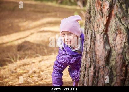 Un bambino guarda fuori da dietro un albero in un giorno di autunno. Foto Stock