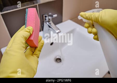 Pulizia nella toilette pubblica del ristorante una mano di uomo in guanti gialli pulisce il lavabo con una spugna Foto Stock