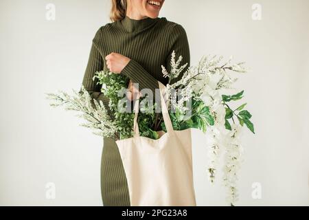 Felice giovane donna che tiene il sacchetto del panno dei fiori bianchi e verdi Foto Stock