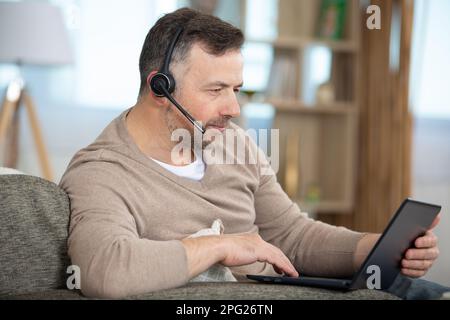 uomo in cuffia seduto sul divano di lavoro al computer portatile Foto Stock