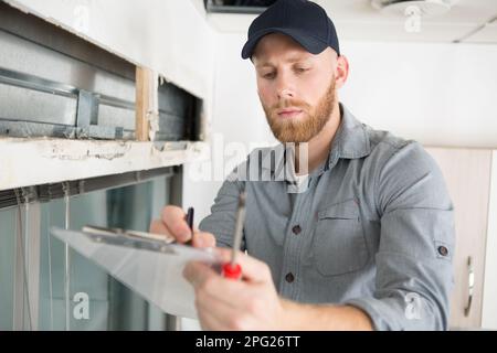 ispettore domestico su una scala mentre scrive su una clipboard Foto Stock