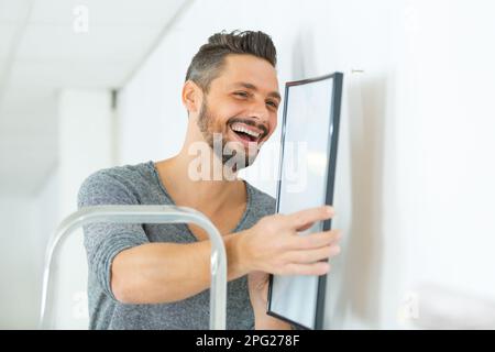 Repairman mettendo cornice immagine sulla parete Foto Stock