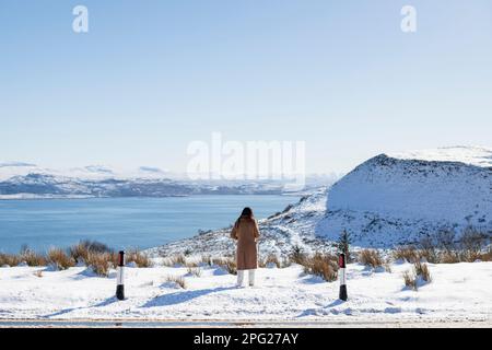 Donna che guarda fuori su un paesaggio scozzese innevato negli altopiani Foto Stock