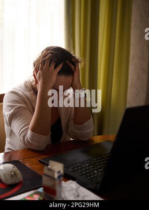 Donna che lavora in multitasking con le mani in mano, sente mal di testa e stanchezza mentre lavora su un notebook Foto Stock