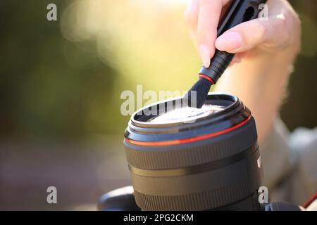 Primo piano ritratto di un fotografo che pulisce l'obiettivo della fotocamera con spazzola all'aperto Foto Stock