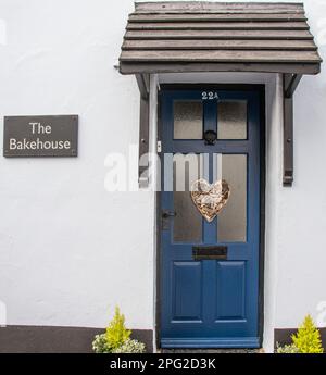 Una porta dipinta di blu con pannelli in vetro, portico in legno e decorazione a cuore. Il nome della casa è il Bakehouse. Foto Stock