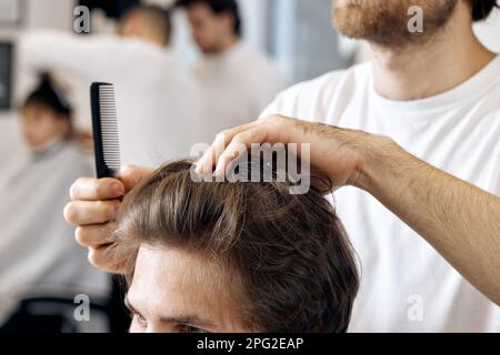 primo piano, professionale hairstylist maschile pettinare i capelli dei giovani clienti Foto Stock