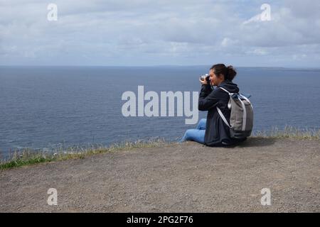 Giovane donna che fotografa le scogliere di Moher, irlanda Foto Stock