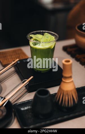 Tè verde Matcha in una tazza di plastica. Vita morta con gli accessori biologici giapponesi Matcha tradizionali sul tavolo. Foto Stock