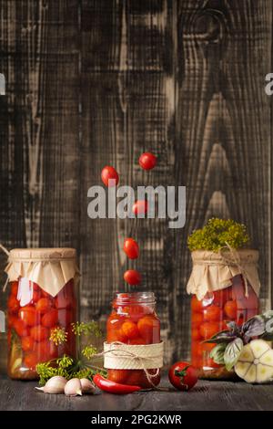 Pomodori caserecci in scatola. I pomodori cadono in un vaso su uno sfondo di legno con spazio per il testo. Un vaso aperto con pomodori ciliegini che volano in esso. Foto Stock