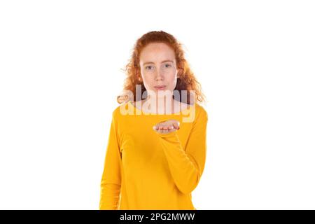 Donna felice con capelli rossi soffiare aria bacio, isolato su giallo Foto Stock