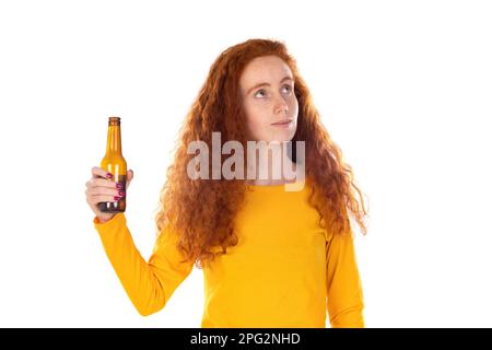 Giovane donna rossa sul muro bianco tenendo la bottiglia di birra felice con un grande sorriso Foto Stock