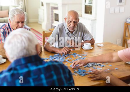 Gruppo concentrato di diversi amici anziani seduti a tavola facendo puzzle insieme Foto Stock