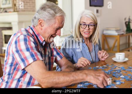 Amici anziani caucasici felici seduti al tavolo facendo puzzle insieme Foto Stock