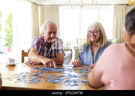 Felice gruppo di diversi amici anziani seduti al tavolo facendo puzzle insieme Foto Stock