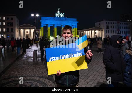 24.02.2023, Berlino, Germania, Europa - protesta con un segno di protesta e una bandiera mostra la sua solidarietà con l'Ucraina di fronte alla porta di Brandeburgo. Foto Stock
