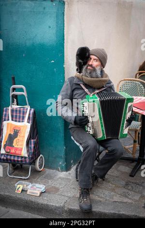 Busker francese parigino con fisarmonica con un gatto nero sulla spalla e borsa 'chat noir', suona nella piazza degli artisti Place du Tertre a Montmartre Foto Stock