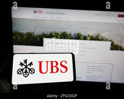 Persona che tiene uno smartphone con il logo della società bancaria svizzera UBS Group AG sullo schermo di fronte al sito Web. Messa a fuoco sul display del telefono. Foto Stock