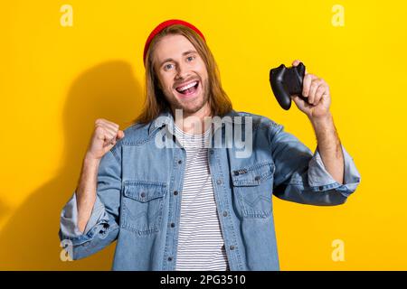 Foto dell'uomo funky fortunato indossare giacca denim crescente pugno vincente gioco playstation isolato sfondo di colore giallo Foto Stock