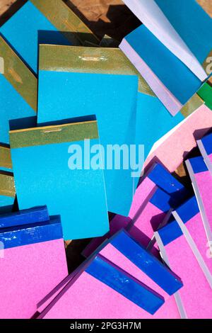 Molti piccoli notepads economici in un heap sudicio, vista dall'alto. Un mucchio di semplici graffietti blu e rosa conservati in un magazzino Foto Stock