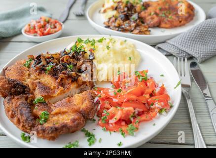 Cotoletta impanata con cipolla arrosto, purè di patate e insalata di pomodoro su un piatto. Foto Stock