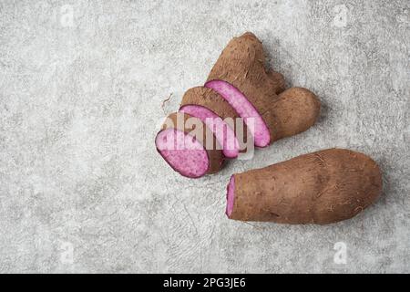 setta di yam viola su una superficie testurizzata bianca, dioscorea alata, aka ube, yam viola, acqua o più grande yam, tuberi viola-carnosa utilizzati in cucina Foto Stock