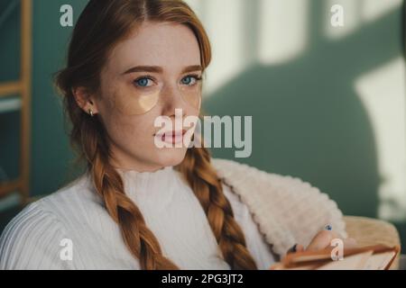 Primo piano ritratto di una giovane donna piacevole seduta sul divano e pensando mentre scrive nel suo notebook. Processo creativo Foto Stock