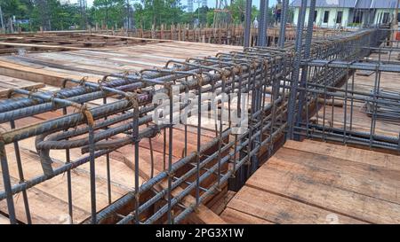 Lavoratore di costruzione che stringe i tondini di acciaio di rinforzo in cantiere. Foto Stock