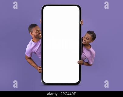 Allegra coppia nera che si nasconde dietro lo smartphone Big Blank Foto Stock