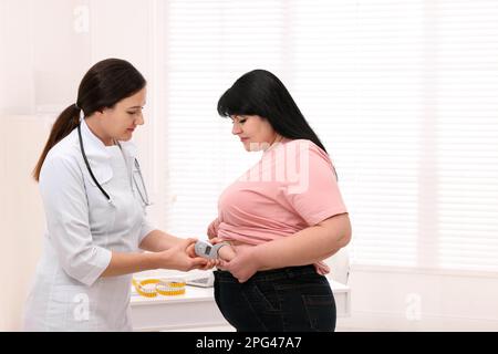 Nutrizionista che misura lo strato di grasso corporeo della donna in sovrappeso con calibro in clinica Foto Stock