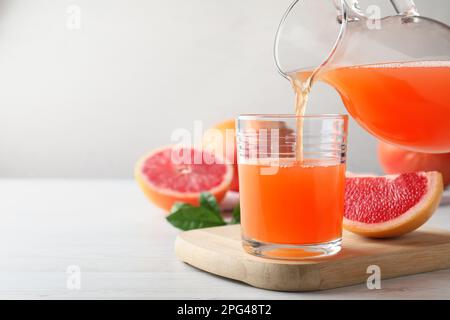 Versare il gustoso succo di pompelmo appena sfornato nel bicchiere su un tavolo di legno bianco. Spazio per il testo Foto Stock