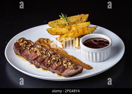 Primo piano di un piatto contenente un pezzo di carne alla griglia e un lato di patatine fritte dorate Foto Stock